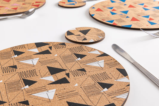 A dining table with place settings. Each place setting is a cork placemat, screenprinted with a 1950's inspired pattern design. Colourful and stylish.