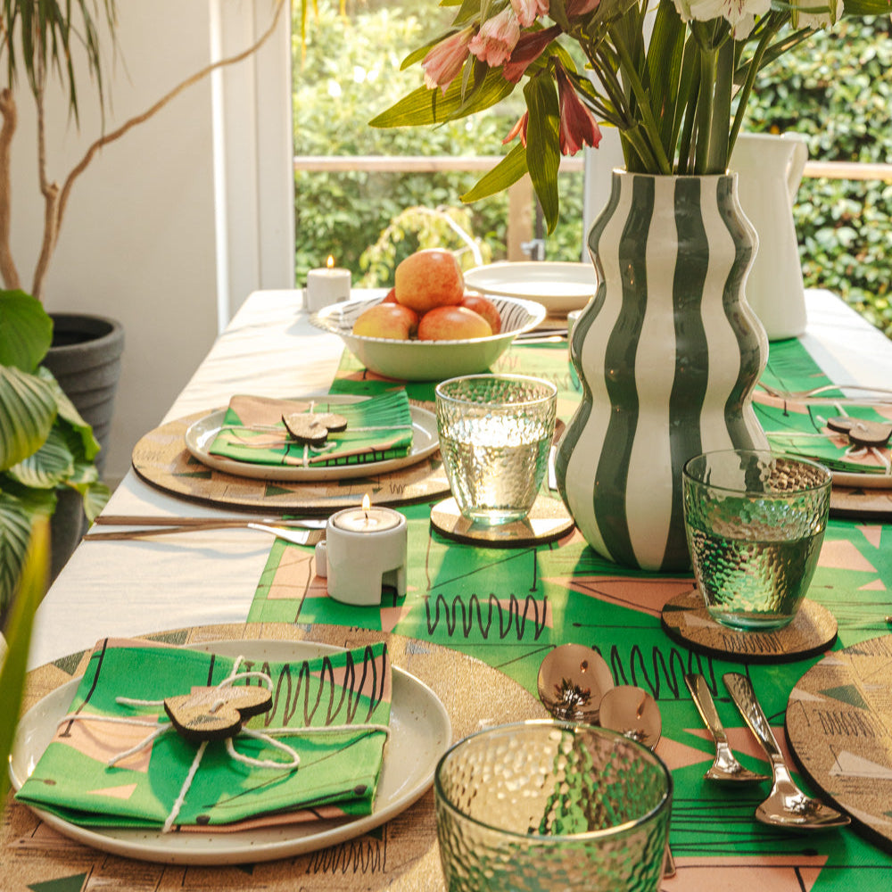 Design led table setting with green tablecloth, cork placemats and coasters and decorative elements. Midcentury inspired.