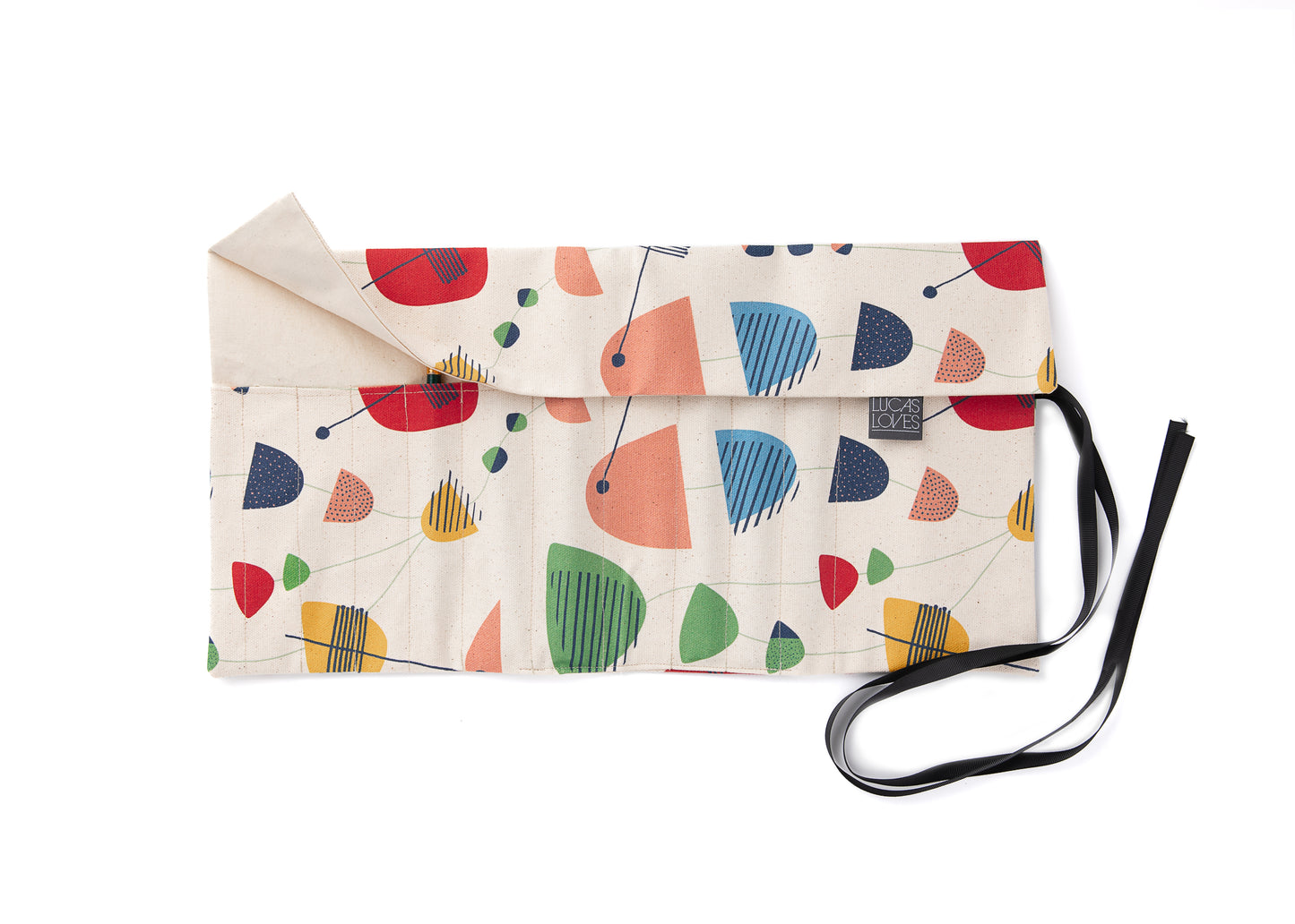 A fabric brush roll with a colorful geometric mid century inspired pattern, featuring various colourful shapes and a ribbon closure to the side.
