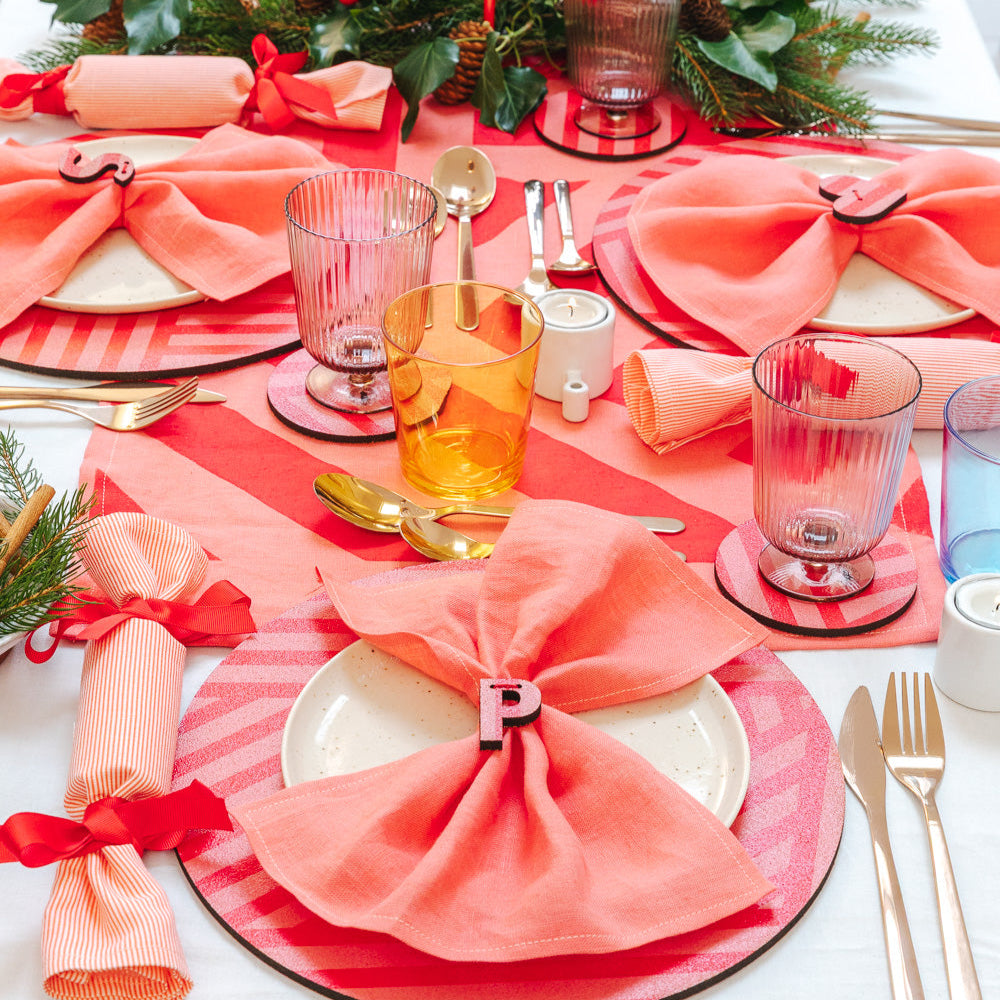 Decorative Christmas table setting with pink and red candy striped cork placemats, coasters, napkins and red accents.