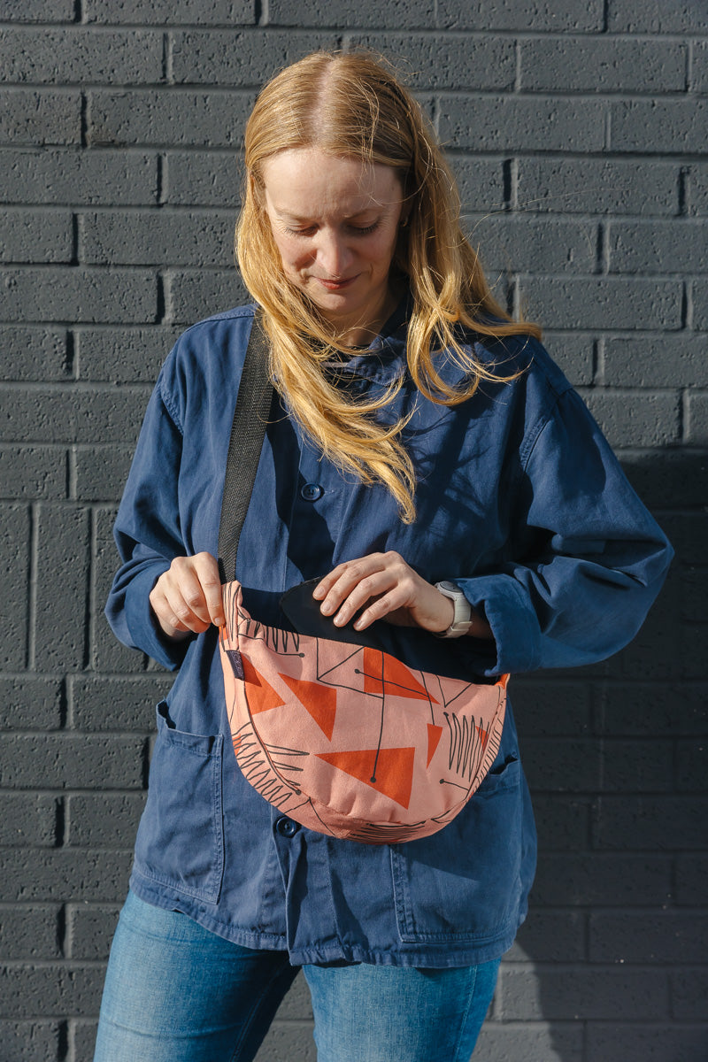 Person wearing a blue jacket with a patterned small cross body bag against a grey brick wall