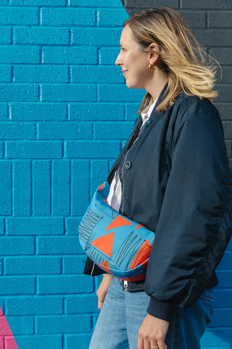 Woman holding a blue and orange bag against a blue brick wall