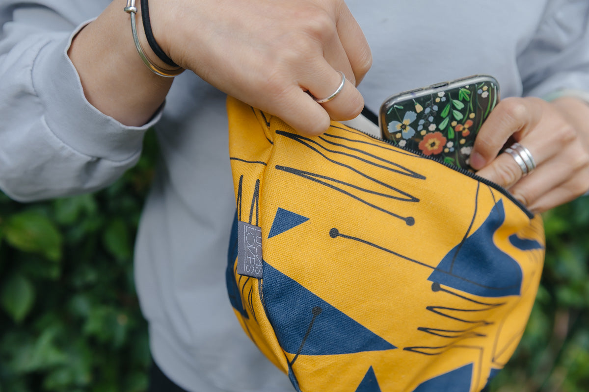 Person holding a yellow pouch with blue patterns, opening it to reveal a floral-patterned phone case.
