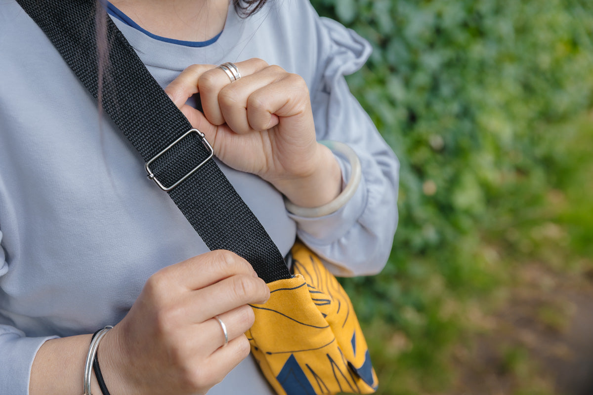 Person adjusting a black strap on a yellow travel small cross body bag